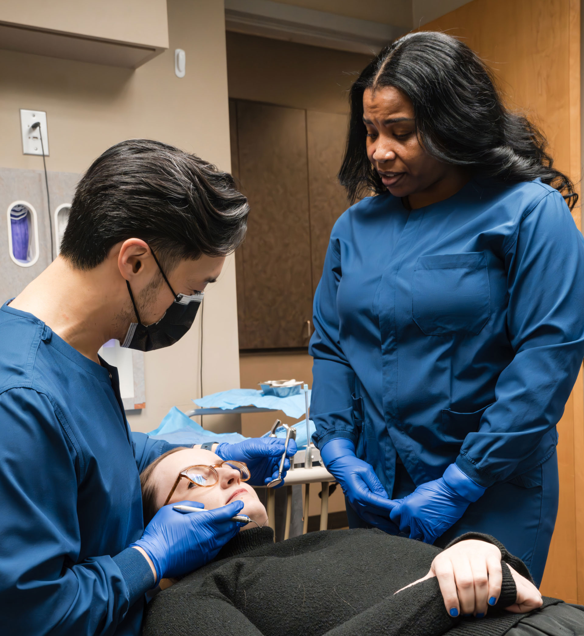 Dr. Chan performing dental exam on patient in dental chair with assistant watching